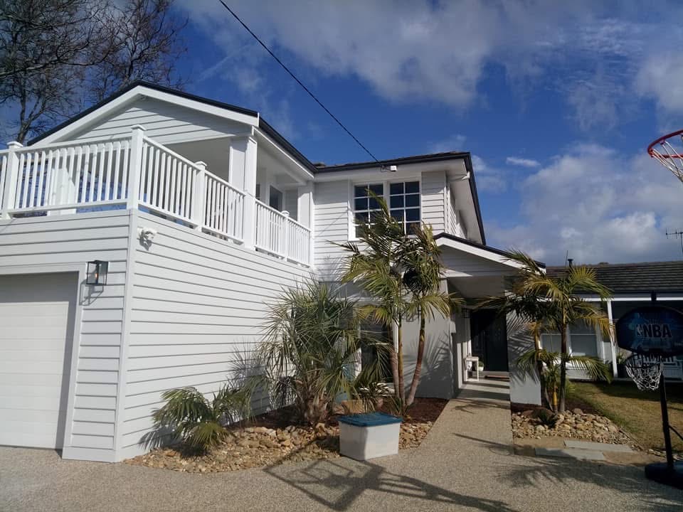 Bright white coastal home with balcony and palm trees after AquaZen repaint